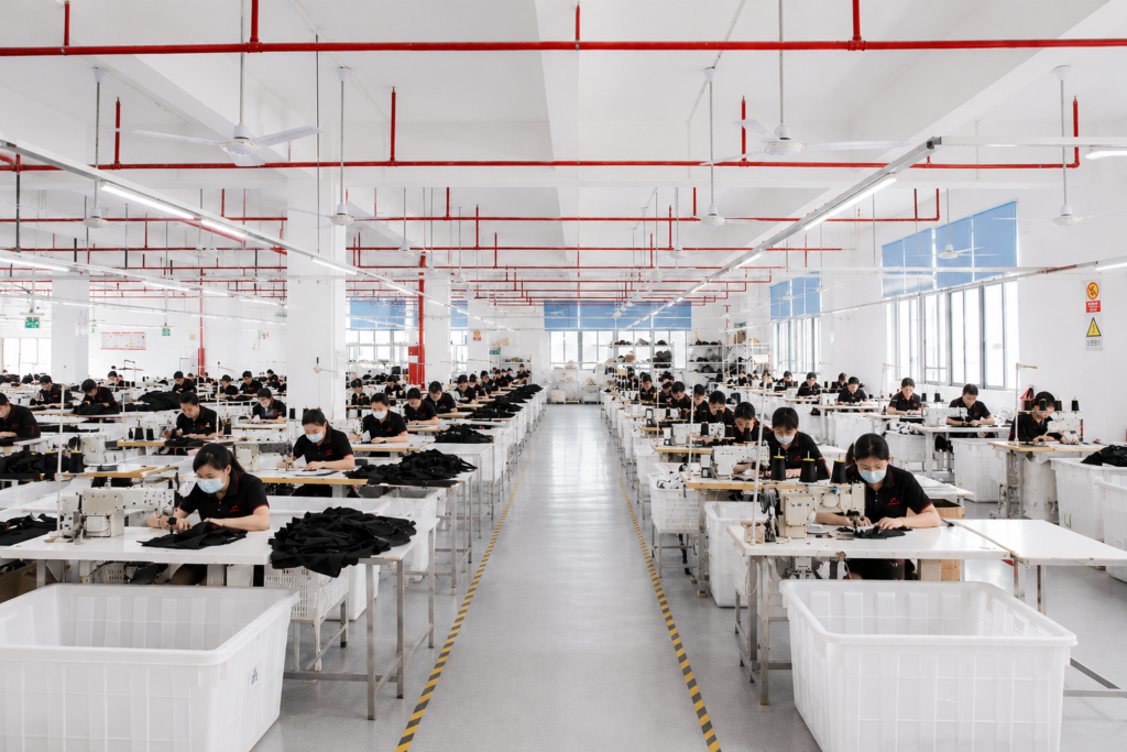 High-volume production workshop with multiple workstations and employees stitching bags under bright lighting