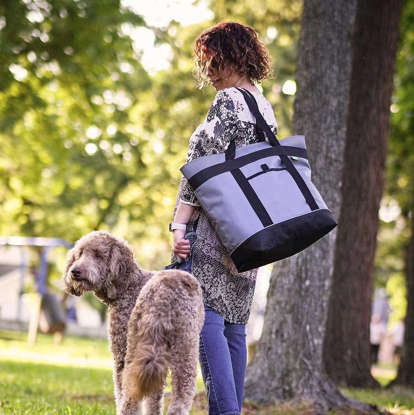 woman carrying cooler tote while walking a dog outdoors