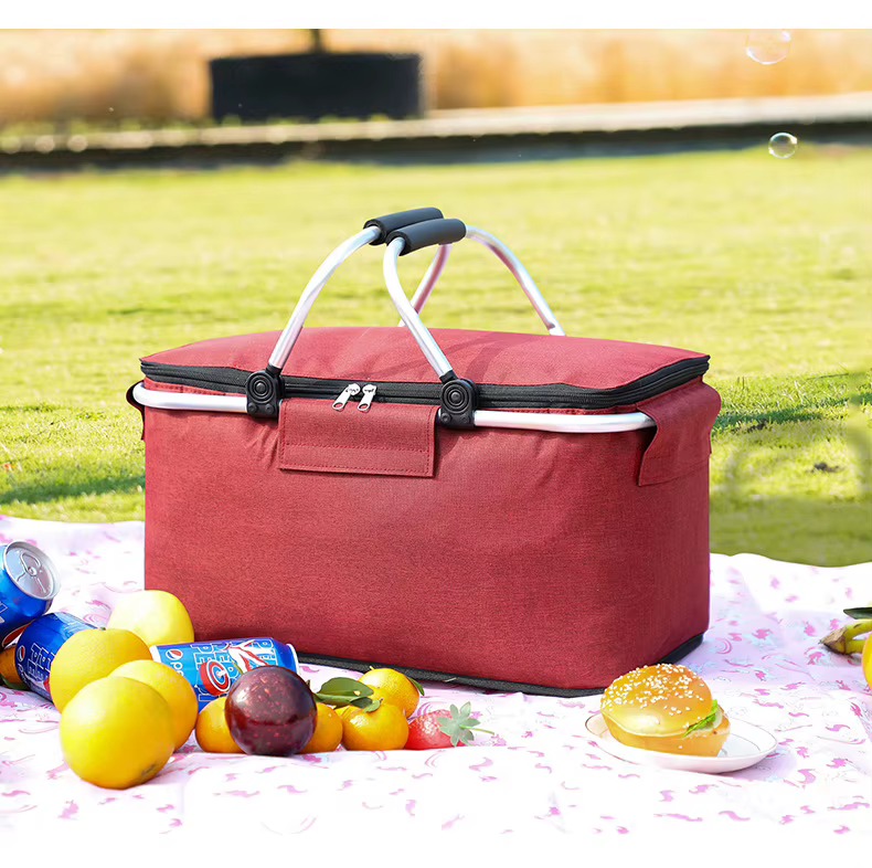red foldable picnic basket on grass with fruit and canned drinks