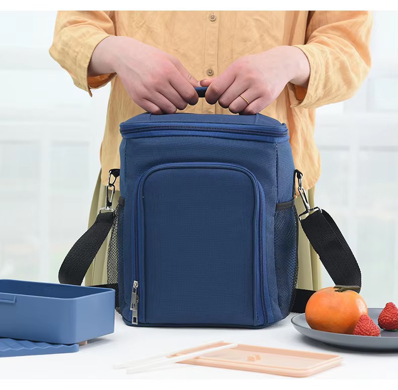 model holding navy blue bag with front pocket packed with a lunch box and utensils nearby