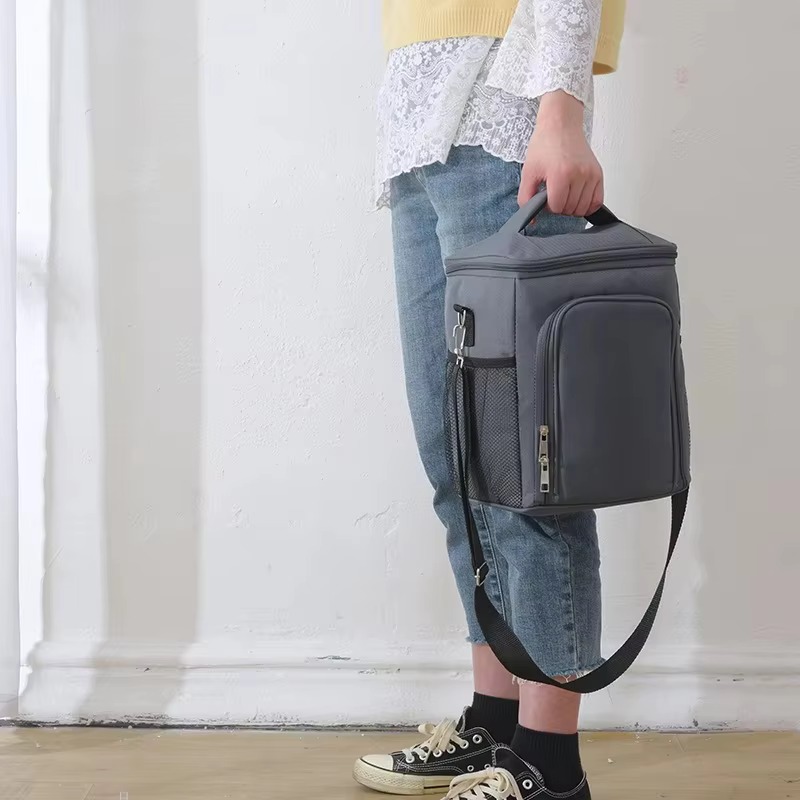 model carrying gray bag by top handle with shoulder strap hanging