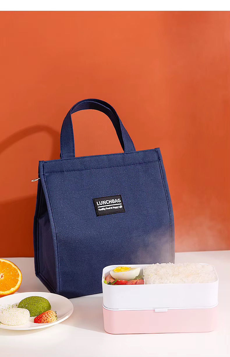 navy bag standing on table beside orange and lunch box on gradient background