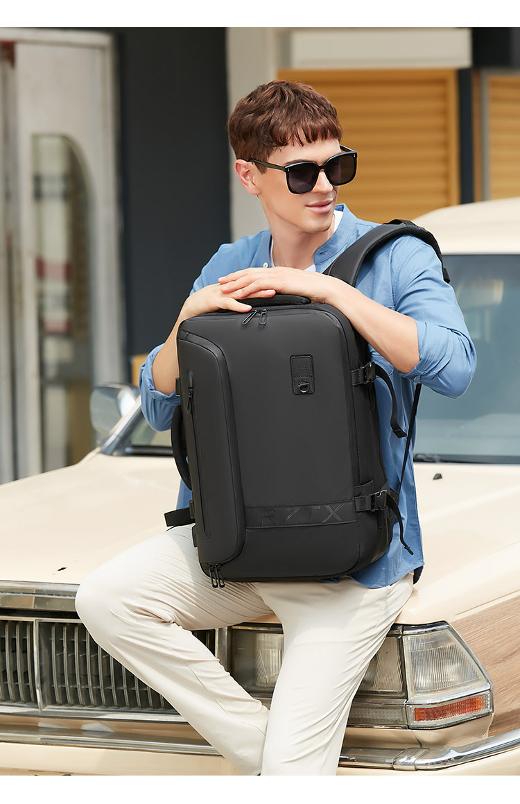 model holding the backpack by its top handle beside a vintage car