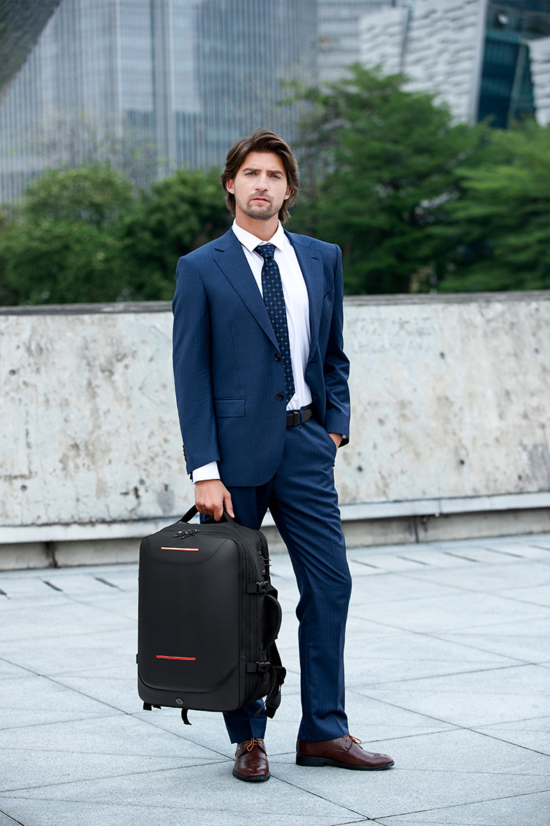 man in a suit holding the backpack by its top handle